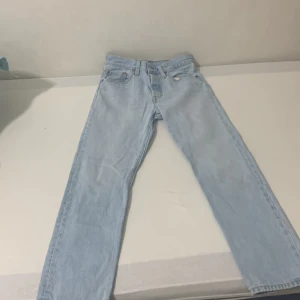 Levi's 501 ljusblå jeans straight fit - Klassiska Levi's 501 jeans i ljusblå denim med rak passform. Byxorna har fem fickor, knappgylf och den ikoniska läderpatchen bak i midjan. Perfekta för dig som gillar en tidlös och avslappnad look.