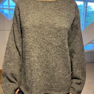 Mörkgrå stickad tröja med öppen rygg - Mysig mörkgrå stickad tröja med oversized passform och långa ärmar. Tröjan har en snygg öppen rygg med en tunn rem upptill som detalj🩵