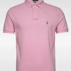 Ljusrosa polo pike från Ralph Lauren - Snygg ljusrosa polo t-shirt från Ralph Lauren med klassisk krage och korta ärmar. T-shirten har blå broderad logga på bröstet och är gjord i mjuk bomull. Perfekt för dig som gillar stilren och chill look.