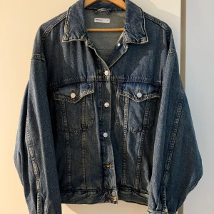 Oversized jeansjacka från Ginatricot - Snygg oversized jeansjacka från Weekday i klassisk mörkblå denim. Jackan har stora bröstfickor med knappar, silverfärgade detaljer och fickor på sidorna. Perfekt att slänga över en hoodie eller t-shirt för en chill look.