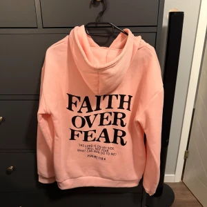 Ljusrosa hoodie med tryck stl S - Säljer en ljusrosa hoodie i stl S med svart texten 'Faith Over Fear' både fram och bak. Tröjan har huva med snörning och en stor magficka. Mjuk och skön, perfekt för kyliga dagar. Enkel och stilren design som sticker ut med sitt budskap. Använt max 1 gång.
