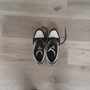 Svarta och vita high top sneakers - Säljer ett par svarta och vita high top sneakers från H&M i storlek 40. Skorna har klassisk snörning, perforerad tå och kontrastpaneler i syntetmaterial. Perfekta för dig som gillar en sportig och stilren look.