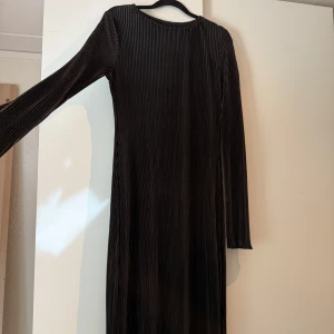 Svart långärmad plisserad klänning - Snygg svart långklänning med plisserat tyg och lång ärm. Klänningen har en rund halsringning, perfekt för dig som gillar stilrena och eleganta plagg. Klänningen är helt oanvänd.