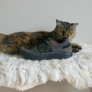 Bruna Five Ten sneakers i mocka - Snygga bruna sneakers från Five Ten med robust design. Ovandel i mocka och textil, svarta snören och röd detalj på plösen. Sulan är slitstark och har bikakemönster för extra grepp. Perfekta för dig som gillar streetstyle och vill ha något som sticker ut.