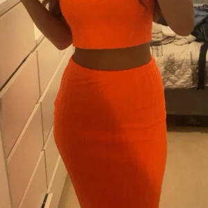 Orange långkjol och tubtop i tight modell - Säljer superfräscha långkjol och tubtop i knallorange färg. De är figurnära och har en enkel, stilren design utan mönster eller detaljer. Perfekt för dig som vill sticka ut med färg och gillar en tight passform.
