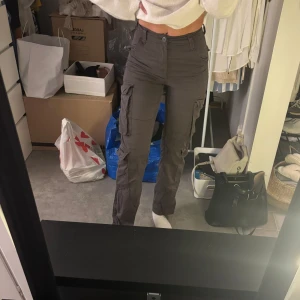 Mörkgråa cargobyxor - Säljer ett par mörkgråa straight fit cargo byxor från Bershka med hög midja och flera praktiska fickor på sidorna.
