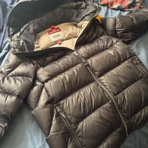Parajumpers dunjacka svart S/ung L - Säljer en autentisk Parajumpers Sheen dunjacka i Svart. Jackan har huva, tvåvägsdragkedja och quiltad design. Perfekt för kalla dagar, med coolt gult detaljband vid axeln. Riktigt snygg och varm jacka för dig som gillar streetstyle.
