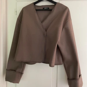 Brun omlottkofta från Gina Tricot - Säljer en brun omlottkofta från Gina Tricot i storlek S. Koftan har v-ringning, vida uppvikta ärmar. Den är lite croppad och tunt material. Vet ej fraktkostnaden.