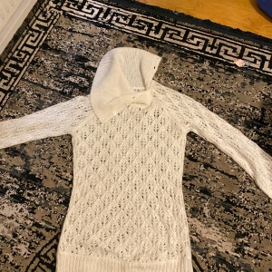 Vit stickad tröja med huva från Bik Bok - Säljer en vit stickad tröja från Bik Bok i storlek L. Tröjan har ett snyggt hålmönster, lång ärm och en unik huva med knappar. Perfekt för dig som gillar mysiga och stilrena plagg med lite extra detaljer.