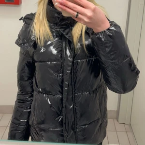 Svart pufferjacka från Calvin Klein - Säljer en svart, glansig pufferjacka från Calvin Klein med hög krage och dragkedja framtill. Jackan har en normal passform och är perfekt för kalla dagar. Diskret CK-logga på bröstet och ärmen. Jackan är långärmad och har en modern look💗