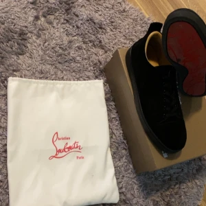 Svarta sneakers från Christian Louboutin  - Stilrena svarta sneakers från Christian Louboutin i mocka med klassisk röd sula. Skorna har rund tå, snörning och diskreta detaljer. Perfekta för dig som vill ha en lyxig och tidlös look med en touch av Paris.