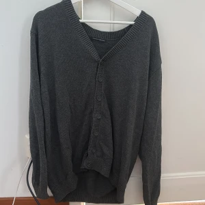 Mörkgrå kofta från Brandy Melville - Säljer en mörkgrå, stickad kofta från Brandy Melville med v-ringad hals och ribbade muddar. Koftan har långa ärmar och knappar framtill. Den är i storleken ”one size” men är ganska stor i modellen och passar många(skriv för mer information)