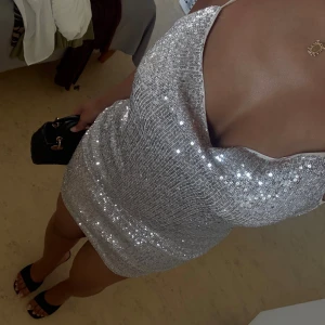 Glittrig silver kortklänning med smala band - Säljer en superfin kort klänning i silver med glittriga paljetter. Klänningen har smala axelband som korsas i ryggen och en snygg draperad urringning framtill. Perfekt för dig som vill sticka ut och glänsa! Passformen är tight och materialet känns festligt.