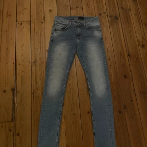 Slim jeans Tiger of Sweden 29/32 - Slimmade jeans från Tiger of Sweden i ljusblå tvätt med snygga slitningar på låren. Klassisk femficksmodell med dragkedjegylf och orangea sömmar. Perfekta för dig som gillar en smal passform och stilren look.