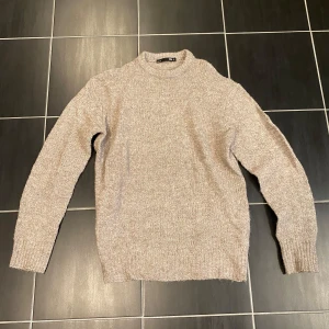 Beige stickad tröja från Lager 157 - Mysig beige stickad tröja från Lager 157 med hög hals och lång ärm. Perfekt för lager-på-lager och chill dagar. Enkel och stilren design som passar till det mesta. Ribbstickade muddar vid ärmslut och nederkant ger en snygg finish. Mycket bra skick!