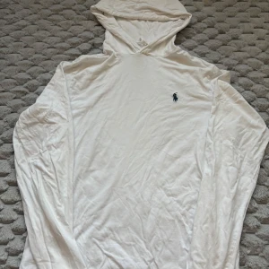 Ralph Lauren hoodie - Vit tunn hoodie från Ralph Lauren med klassisk broderad logga på bröstet. Tröjan har långa ärmar, huva och är tillverkad i mjuk bomull. Perfekt för en clean och avslappnad stil.