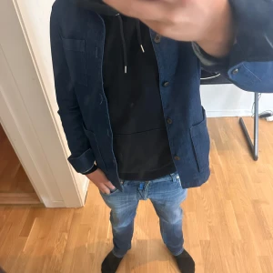 Mörkblå jeansjacka med knappar - Säljer en stilren mörkblå jeansjacka med klassisk passform. Jackan har tre stora fickor framtill och stängs med knappar. Perfekt för dig som gillar en enkel och clean look. Passar till både hoodie och t-shirt. Märke: John Henric strl xs. Personen på bilden är 180cm och 71kg. Mitt pris 699