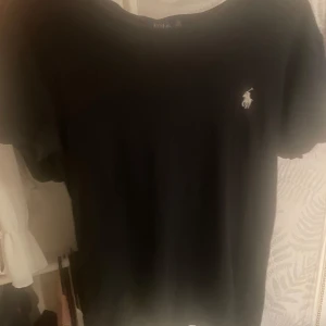 Svart t-shirt från Polo Ralph Lauren - Svart t-shirt från Polo Ralph Lauren med klassisk vit logga broderad på bröstet. Modellen är enkel med rund hals och korta ärmar, perfekt för en clean och stilren look. Materialet känns mjukt och skönt mot huden.