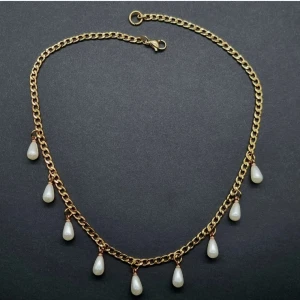 Guldigt halsband med pärldroppar - Snyggt halsband med en kedja i guldton och hängande vita pärldroppar. Kedjan har en klassisk länkdesign och pärlorna är droppformade, vilket ger en elegant och trendig vibe. Perfekt för att lyfta din outfit med lite extra bling och stil.