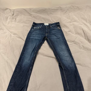 Replay Grover straight fit jeans blå strl 29-32 - Snygga blå jeans från Replay, modell Grover med straight fit. Klassisk femficksdesign, tydliga kontrastsömmar och läderpatch bak i midjan. Jeansen har en mörk tvätt med lätt slitning och är tillverkade i bomull för en skön känsla. My pris ca 1599kr