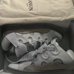 Lanvin curbs - Unika vita sneakers från Lanvin med breda, mönstrade snören i grått och vitt. Skorna har rund tå, perforerade detaljer framtill och coola metallöglor. Tillverkade i Italien i en mix av skinn och syntet. Snygg chunky sula och modern design som sticker ut.