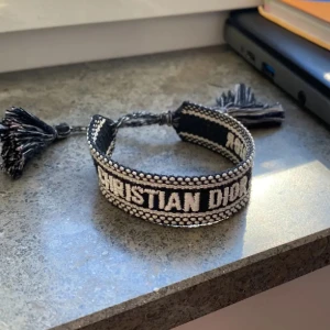  Dior armband - Snyggt vävt armband från Christian Dior i svart och vitt med tydlig logga och dekorativa tofsar i ändarna. Nypris 3500 kr. Mitt pris 1499