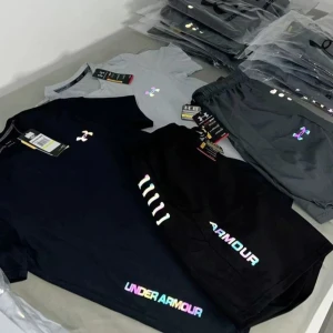 Svart t-shirt från Under Armour - Svart t-shirt från Under Armour med regnbågsskimrande logga på bröstet och texten UNDER ARMOUR i färgglada bokstäver nedtill. Klassisk passform och rund halsringning, perfekt för en sportig look.