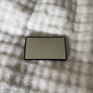 Svart sminkspegel i kompakt format - En stilren, rektangulär sminkspegel med svart plastfodral. Perfekt storlek för att ha i väskan eller sminkväskan när du behöver fixa looken snabbt. Spegeln är enkel och praktisk utan extra detaljer.