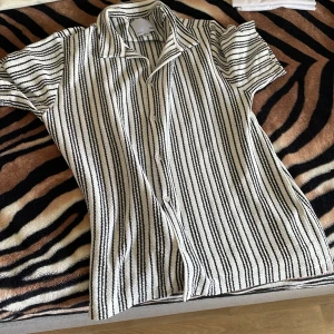 Randig kortärmad skjorta i bomull - Snygg kortärmad skjorta från H&M i vit och svart med vertikala ränder. Skjortan har klassisk krage, knäppning framtill och är gjord i mjuk bomull. Perfekt för en chill och stilren look. Storlek xl men sitter som L 