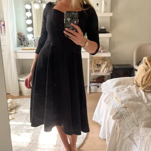 Svart långklänning med öppen rygg - Supersnygg svart långklänning i 100% polyester med trekvartsärm, markerad midja och v-ringad hals. Baksidan har en öppen rygg med en söt rosettdetalj upptill. Klänningen har en elegant och tidlös siluett som ger en chic vibe. 