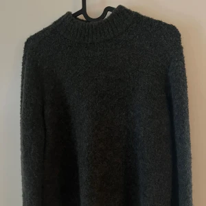 Mörkgrön stickad tröja från STOCKH LM - Perfekt stickad tröja från STOCKH LM med ribbad hög hals och lång ärm. Tröjan har en fluffig struktur och en liten guldfärgad logodetalj vid nederkanten.