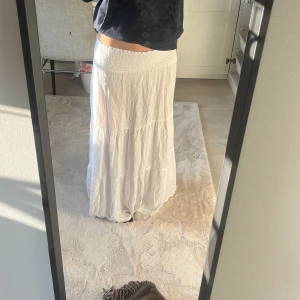 Vit långkjol från lager 157 XS - Luftig och flowy vit långkjol från Etam 1939 i storlek XS. Kjolen har smock i midjan för en bekväm passform och är sydd i flera lager för en bohemisk vibe. Perfekt till varma dagar och enkel att styla med crop tops eller stickade tröjor.