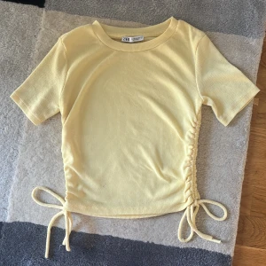 Gul ribbad topp med snörning från Zara - Superfin ljusgul ribbad topp från Zara med korta ärmar och snygg snörning i sidorna som ger en cool, justerbar passform. Oanvänd och somrig!
