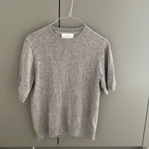 Grå kortärmadstickad tröja från Neo Noir - Mysig grå stickad tröja från Neo Noir med rund halsringning och kortare ärmar. Enkel och stilren design som passar perfekt till jeans eller kjol. Tröjan har en mjuk känsla och ribbade detaljer vid hals och ärmslut. Tröjan är i jättebra skick. Tröjan är storlek S, jag är 174 cm och den passar perfekt. 
