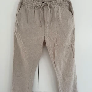Beiga linnebyxor med snörning  - Snygga beiga linnebyxor i storlek L med dragsko i midjan och fickor både fram och bak. Perfekta för varmare dagar. Avslappnad passform och stilren look.