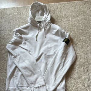 Vit hoodie från Stone Island L - Vit hoodie från Stone Island med klassisk patch på vänster ärm. Storlek L men skulle mer säga att den passar som M. Tröjan har huva med snörning och stor känguruficka framtill.  Ny skick nästan och är köpt i NK för någon månad sedan! 