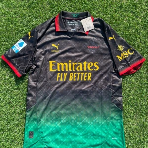 AC Milan Puma x Off-White Leão tröja - AC Milan 2025 special edition fotbollströja i samarbete mellan Puma och Off-White. Svart och grön med gula tryck, röda detaljer på krage och ärmslut. Nummer 10 och 'RAFA LEÃO' på ryggen. Tillverkad i lätt funktionsmaterial med diskret mönster och klassisk krage.