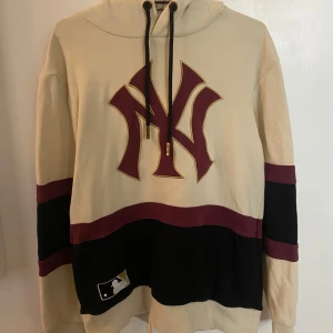 VINTAGE Majestic Yankees hoodie beige vinröd S - Snygg vintage hoodie från Majestic Athletic med New York Yankees-logga framtill och 'New York' på ryggen. Beige bas med vinröda och svarta detaljer, huva med snörning och breda kontrastpaneler. Perfekt för dig som gillar sportig streetstyle. PRIS GÅR ATT DISKUTERA