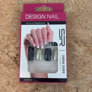 Designnaglar från Sabrina Rudnik - Set med 12 stycken lösnaglar i svart och glittrigt guld. Naglarna har en rektangulär form och kommer med nagellim(vet inte om nagellimmet funkar) Perfekt för dig som vill ha en snygg och trendig look utan att behöva gå till salong.