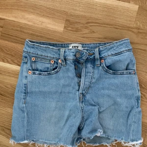 Ljusblå jeansshorts från 157 - Snygga ljusblå jeansshorts från 157 med råa kanter och klassisk femficksdesign. Shortsen har hög midja, knappar framtill och är gjorda i mjukt denim. Perfekta för varma dagar och en avslappnad stil.