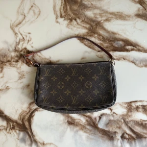 Louis Vuitton monogram axelväska - Säljer en klassisk Louis Vuitton axelväska i brunt med ikoniskt monogrammönster och guldfärgade detaljer. Väskan har en smidig dragkedja och en tunn axelrem i läder. Perfekt storlek för det viktigaste och en riktig statement piece.