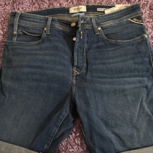 Blå jeansshorts från Replay - Snygga blå jeansshorts från Replay med klassisk femficksdesign och gul kontrastsöm. Modellen har upprullade benslut och normal passform. Perfekta för en avslappnad stil och funkar till det mesta. Märkesdetaljer på bakfickorna och etikett bak i midjan.