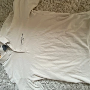 Beige pikétröja från H&M Relaxed - Snygg beige pikétröja från H&M Relaxed med klassisk krage och knäppning framtill. Broderad text på bröstet med Paris-detalj. Skön bomullskänsla och avslappnad passform, perfekt till jeans eller shorts.