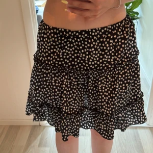 Svart blommig volangkjol från SHEIN - Supersöt svart kortkjol från SHEIN med vita blommor och volangdetaljer. Kjolen har en flowy passform och elastisk midja som gör den bekväm och lätt att bära.