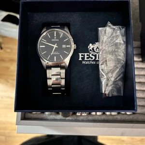 Silverfärgad Festina herrklocka - Stilren klocka från Festina med svart urtavla och datumvisning. Armbandet är i blankt silverfärgat metall och klockan har en klassisk rund form. Perfekt accessoar för dig som gillar en clean och tidlös look. Tyvärr lite repig därav kan priset diskuteras 