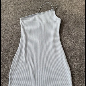 Ljusgrå ribbad one shoulder klänning - Snygg ljusgrå ribbad klänning med one shoulder och smala axelband. Kort modell som sitter figurnära och har en stilren, minimalistisk look. Perfekt för dig som gillar trendiga och enkla plagg.