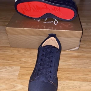 Mörkblå sneakers från Christian Louboutin - Snygga mörkblå sneakers från Christian Louboutin med klassisk röd sula och broderad logga på hälen. Skorna är i mocka och textil, har rund tå och snörning framtill. Perfekt för dig som vill sticka ut med exklusiva detaljer och lyxig känsla.