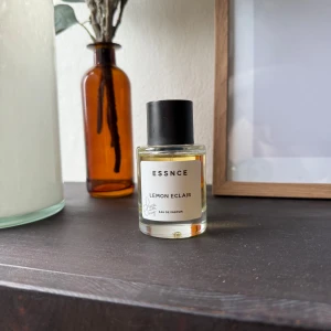 ESSNCE Lemon Eclair parfym - Fräsch parfym från ESSNCE med doften Lemon Eclair. Kommer i en stilren, rund glasflaska med svart lock och vit etikett. Perfekt för dig som gillar citrus och söta toner. Eau de Parfum-variant som håller länge. (Använda fåtal gånger)