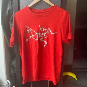 Röd Arc'teryx t-shirt - Röd t-shirt från Arc'teryx med ikoniskt vitt skelett-tryck på bröstet. Klassisk passform med rund hals och korta ärmar. Tillverkad i mjuk bomull som känns skön mot huden. Perfekt för dig som gillar outdoor-vibbar och stilren design.