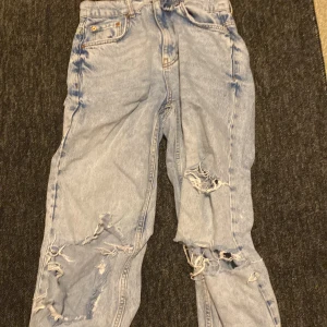 Ljusblå ripped jeans med loose fit - Säljer ett par ljusblå jeans med rejält slitna och trasiga detaljer på benen. Jeansen har en loose passform och klassisk femficksdesign. Perfekta för dig som gillar en avslappnad och edgy stil.